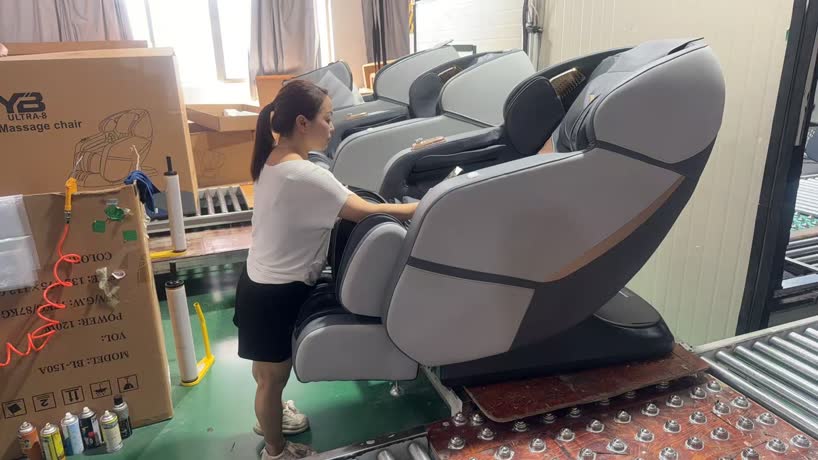עובדת מרכיבה כורסת מסאז' YB ULTRA-8 לצד ארגזי המשלוח במפעל